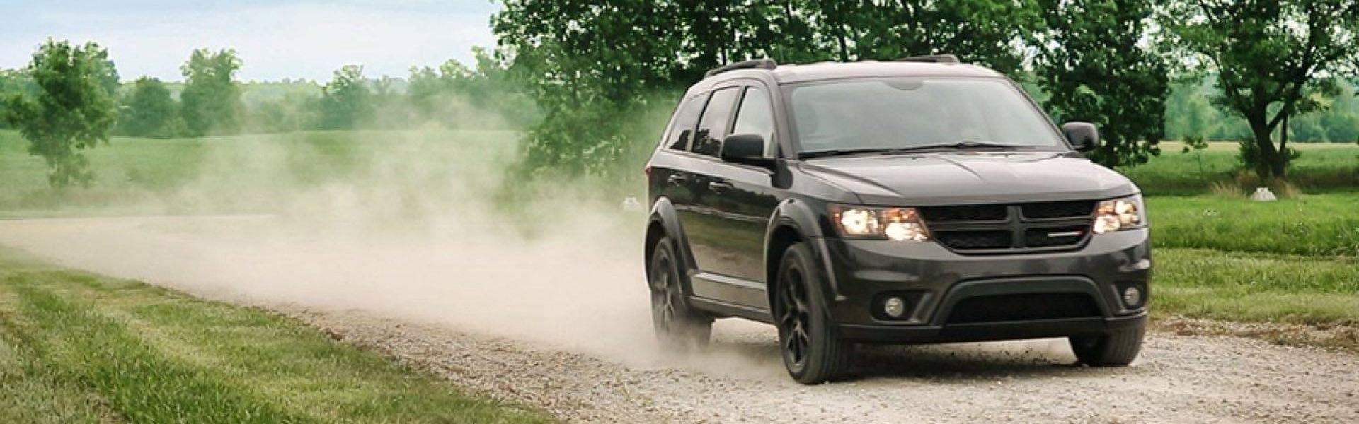 Gray Dodge Journey driving through the dirt road and kick up dirt along the way