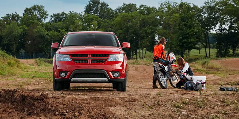 Red Dodge Journey parked in the park while two people get ready to use their dirt bike