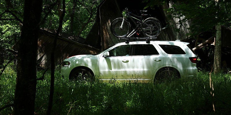 White Dodge Durango parked in a tall grass field with bikes attached to the top of the car