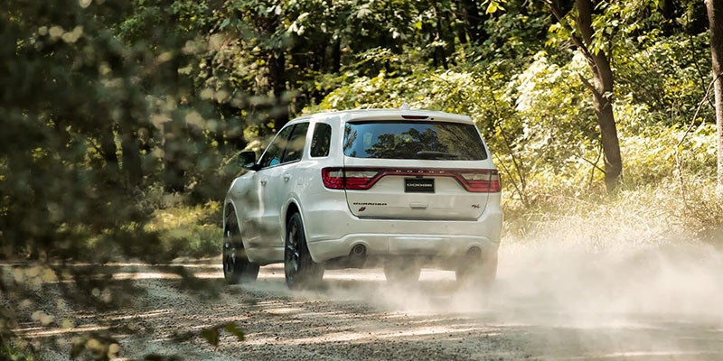 White Dodge Durango driving on dirt road and kicking up dirt in the process