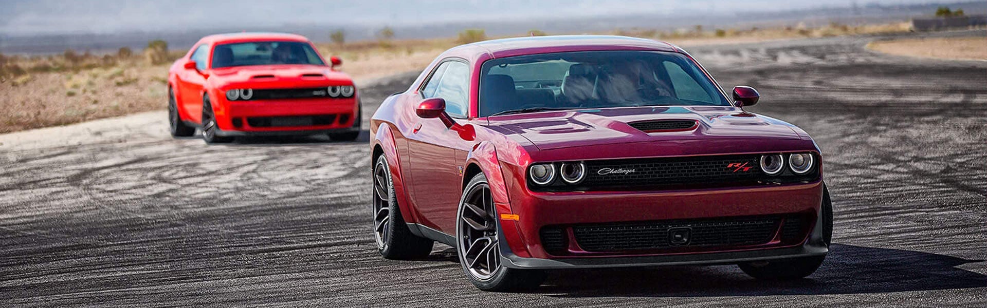 Two Red Challengers racing on a race track on a bright and sunny day