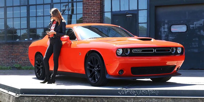 Orange Dodge Challenger parked next to a building as a woman leans over the car while on the phone