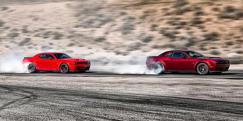 Two Dodge Challengers burning out their tires on the pavement on a sunny day