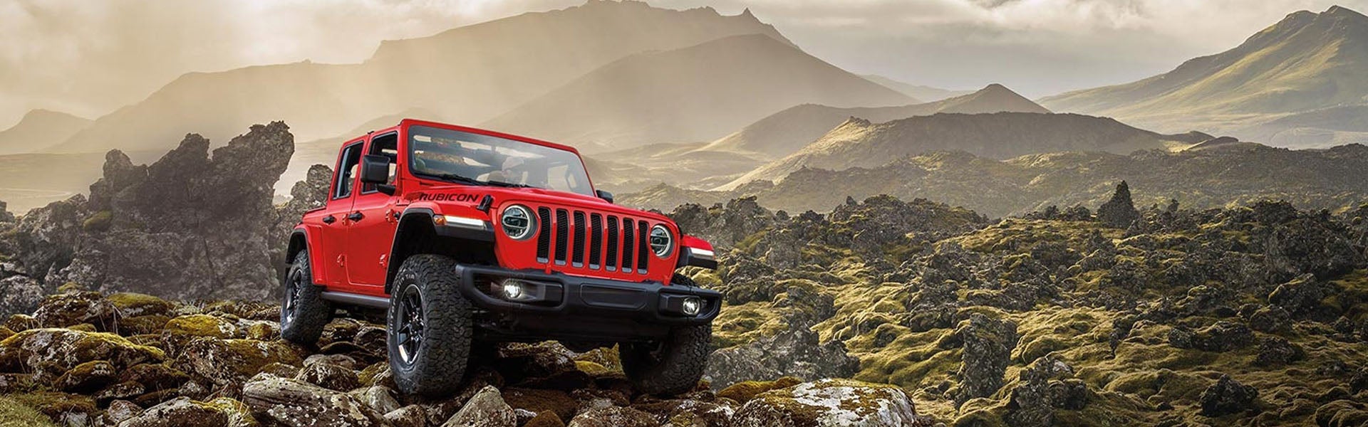 Red Jeep Wrangler parked on a boulder next to a huge mountain
