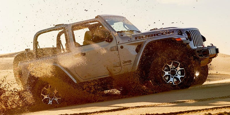 Jeep Wrangler driving in the desert and kicking up sand while the sun sets