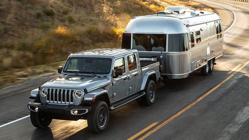 Gray Jeep Gladiator hitching a large rental unit down the road at high speed