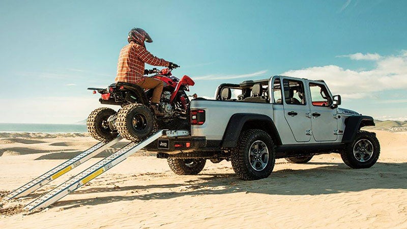 Gray Jeep Gladiator parked on the beach as an ATV is trying to onto the back