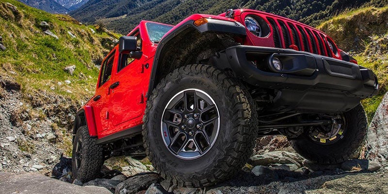 Red Jeep Wrangler driving up boulders on a sunny day outside