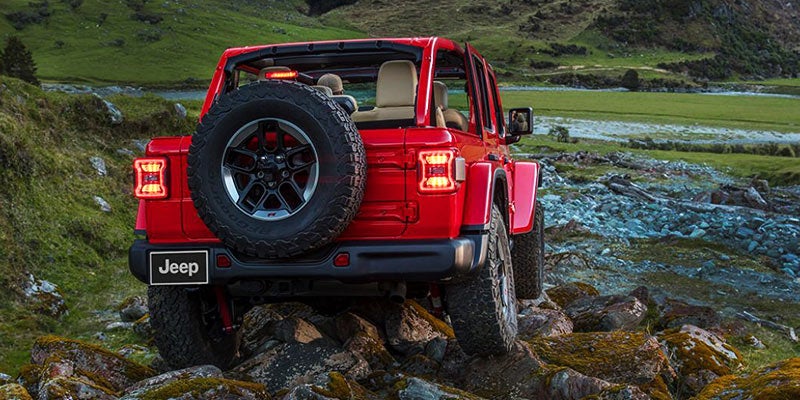 Red Jeep Wrangler Crossing over a bed of rocks next to a large river