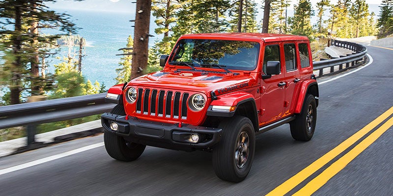 Red Jeep Wrangler driving down the road at high speed next to tall trees