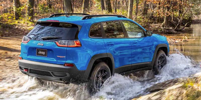 Blue Jeep Cherokee crossing a river during the day in the forest
