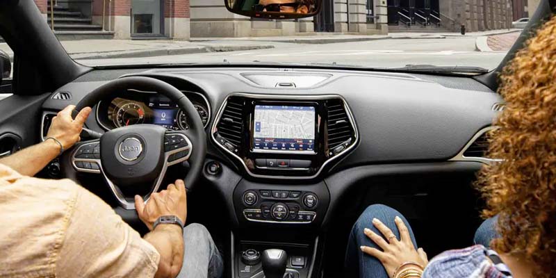 Man and woman sitting inside of their Jeep Cherokee using its tech features