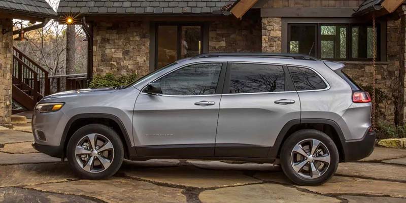 Gray Jeep Cherokee parked on the drive way next to a big house