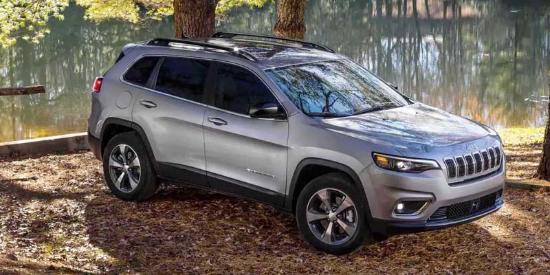 Gray Jeep Cherokee parked next to a river in the middle of the forest