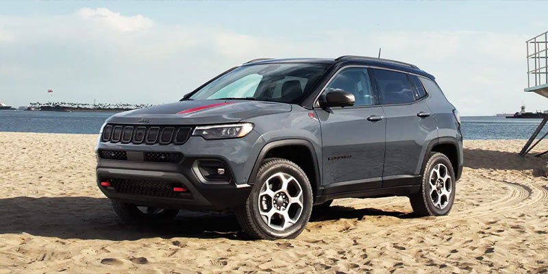 Gray Jeep Compass parked on sandy beach next to an ocean