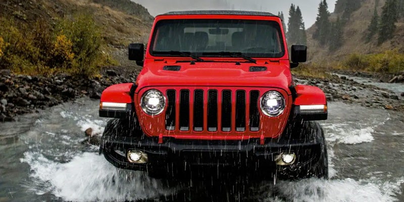 Red Jeep wrangler driving through the river while it is raining outside