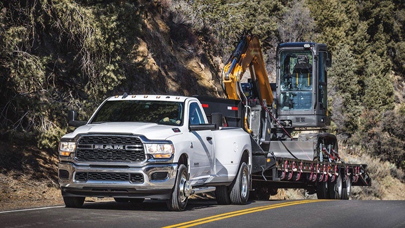 White Ram 3500 hauling a tiny excavators on a sunny day